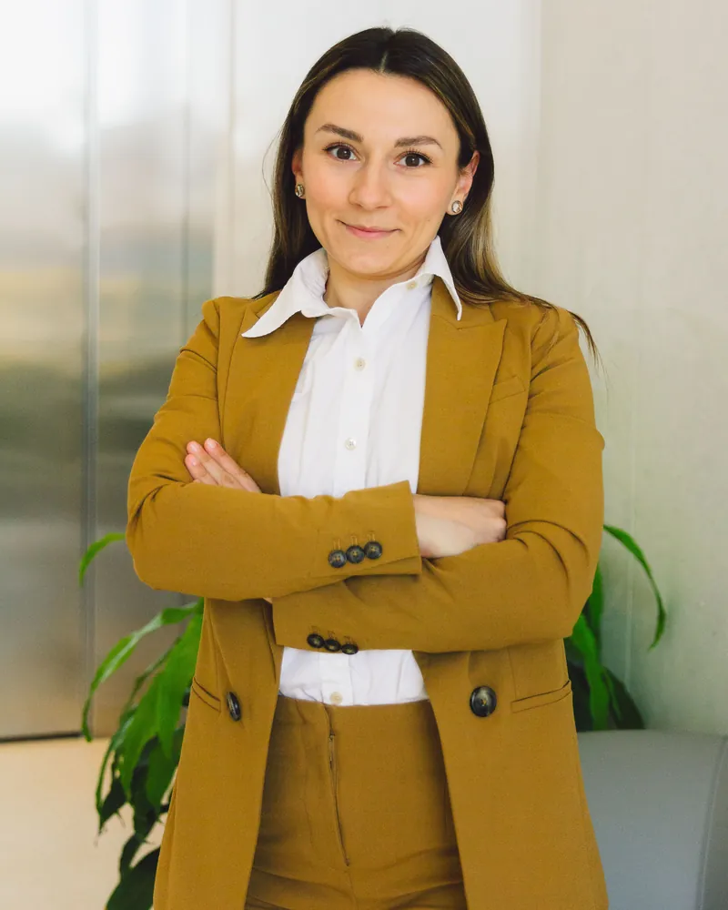 A woman in a mustard suit standing with her arms crossed in an office
